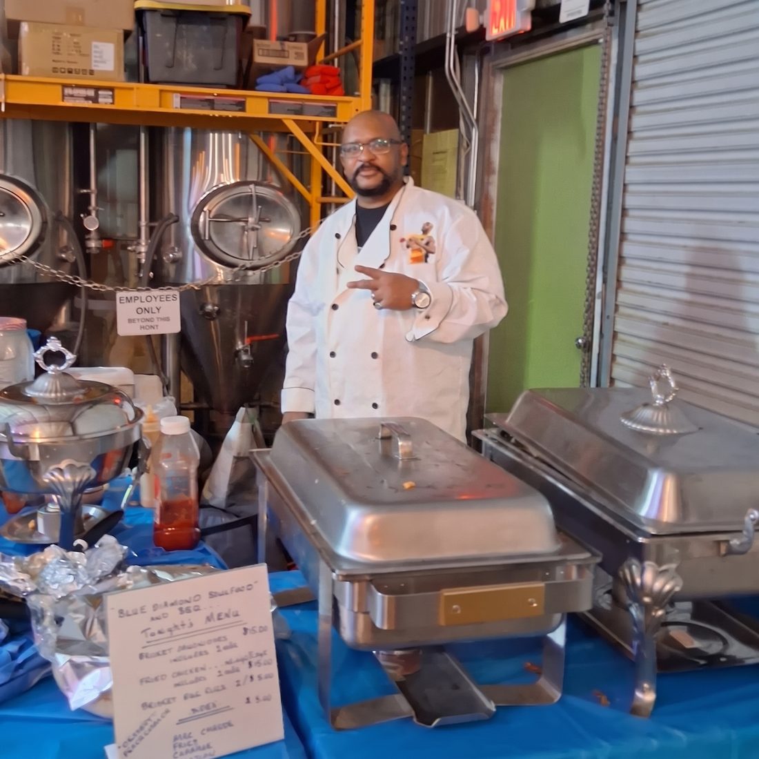 BillyRay Williams in his chef coat, catering an event beside his chafing dishes and handwritten menu